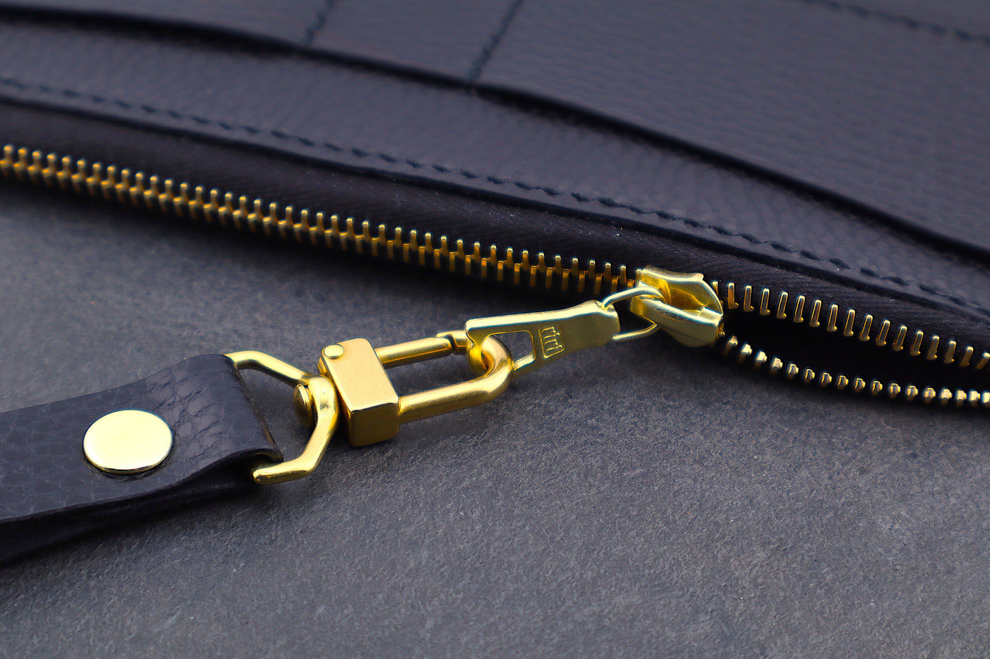 Close-up of a black bag with a gold zipper pull and strap.