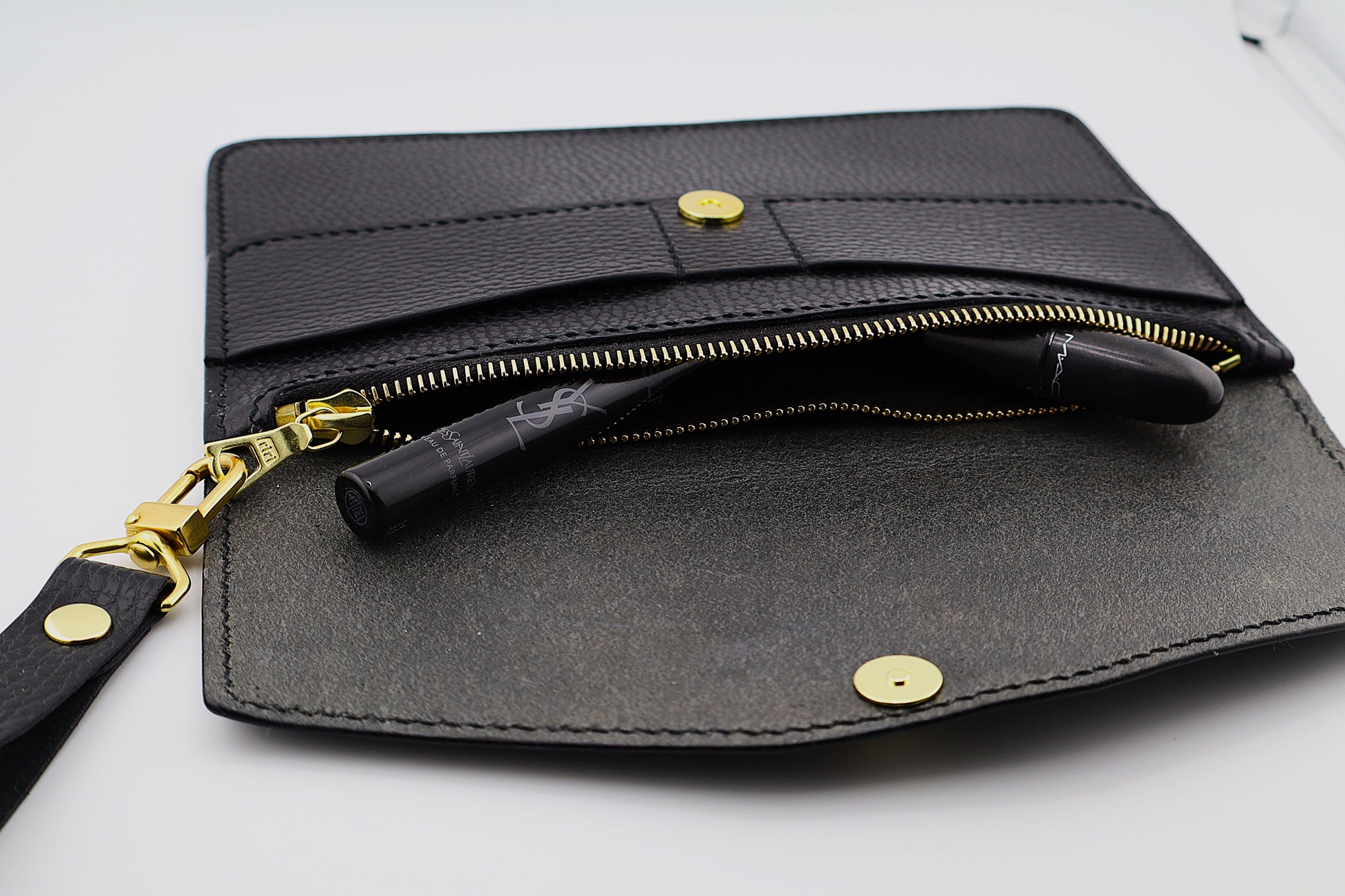 Black leather clutch with gold accents on a white background